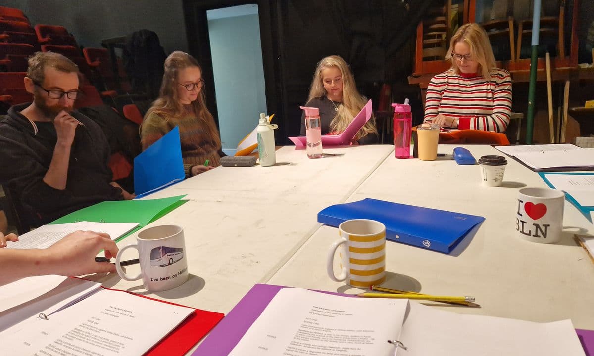 A group of actors sitting around a table reading scripts